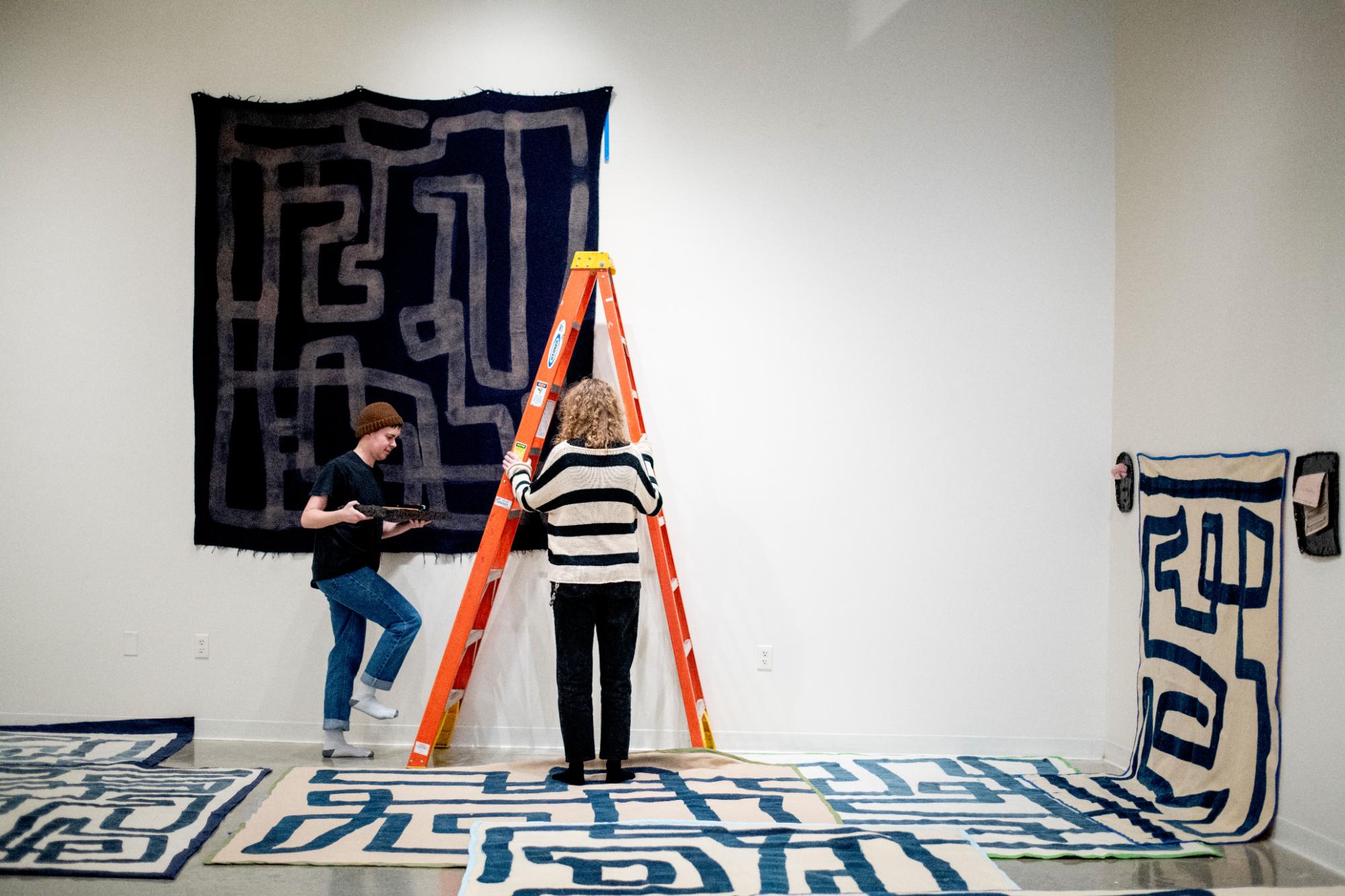 View of Exhibition installation with students going up on a ladder
